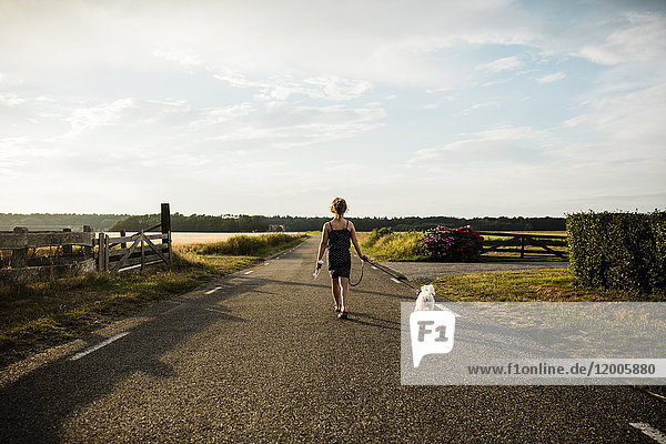 Girl walking with dog on rural road holding miniature wind turbine