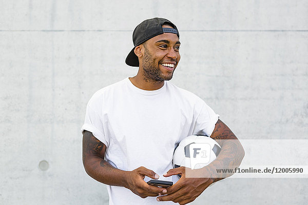 Portrait of laughing young man with soccer ball and cell phone