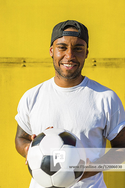 Porträt eines lächelnden Mannes mit Fußball vor gelber Wand