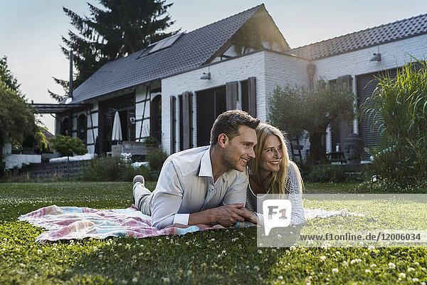 Happy couple lying on grass in the garden of their country house