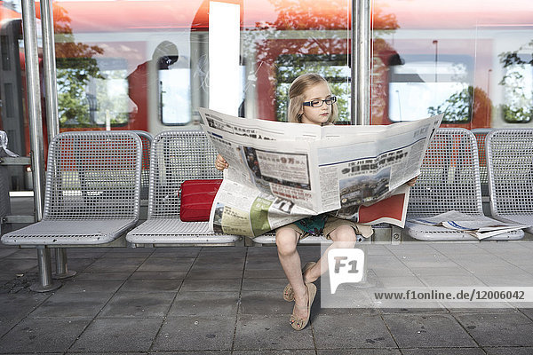 Porträt eines kleinen Mädchens  das am Bahnsteig sitzt und Zeitung liest.