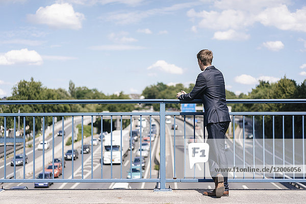 Geschäftsmann steht auf einer Brücke über eine Autobahn