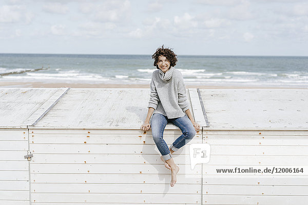 Lächelnde Frau auf Holzkiste am Strand sitzend