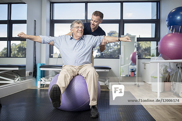 Senior man exercising with fitness ball at physio's practice