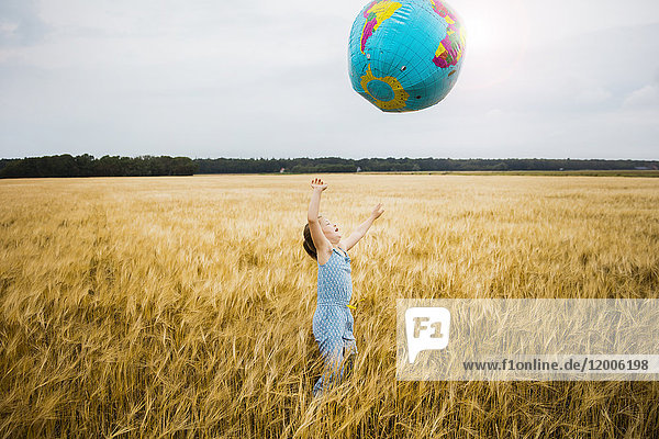 Mädchen steht im Getreidefeld und spielt mit dem Globus