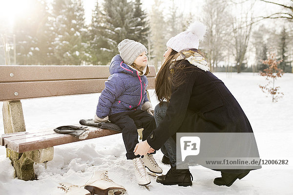 Mother helping daughter to put on her ice skates