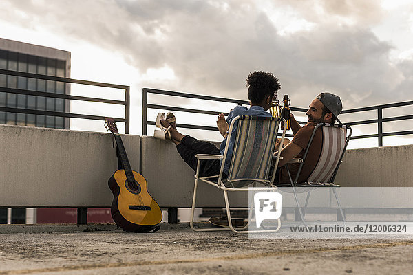 Young couple with beer and guitar sitting on rooftop