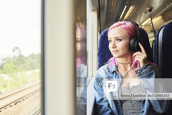 Young woman with pink hair listening to music while traveling by train