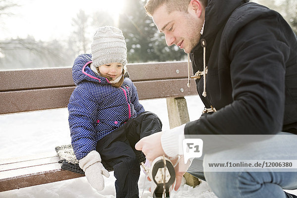 Father helping daughter to put on her ice skates
