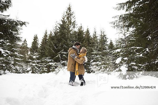 Glückliches junges Paar steht sich in der Winterlandschaft gegenüber