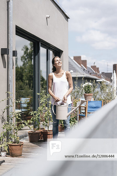 Smiling woman on balcony holding watering can