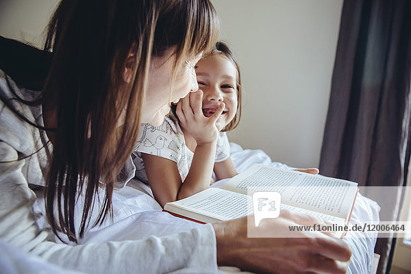 Mutter und Tochter lesen Buch im Bett