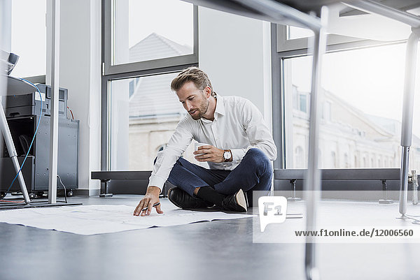 Businessman sitting on the floor of his office looking at construction plan