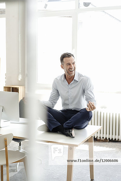 Happy businessman sitting on table in office practising yoga
