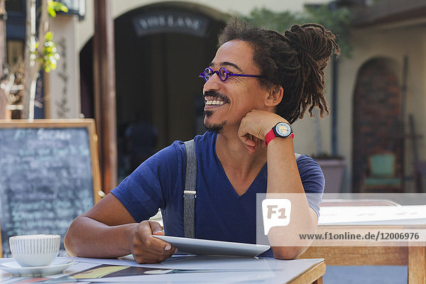 Smiling mixed race man using digital tablet at sidewalk cafe