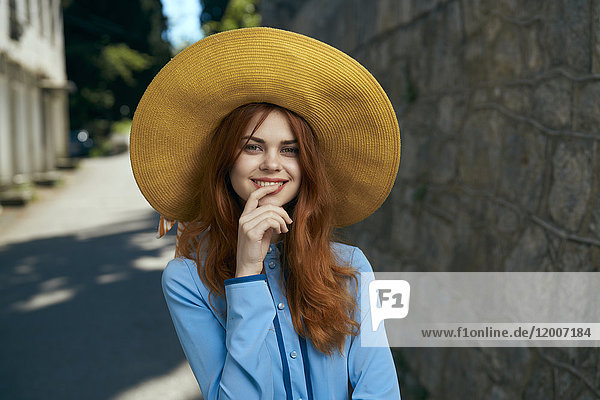 Lächelnde kaukasische Frau mit Hut in der Nähe einer Steinmauer