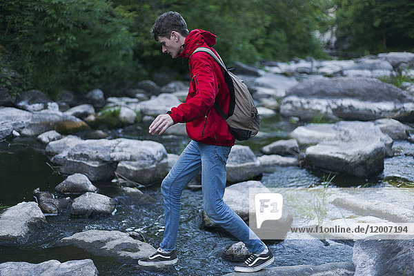 Kaukasischer Mann geht auf Felsen und überquert einen Fluss
