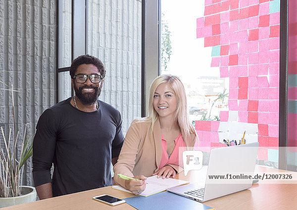 Kreative Geschäftsleute posieren mit Laptop am Tisch
