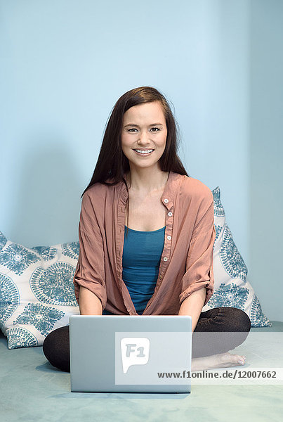 Smiling mixed race woman sitting on bed using laptop