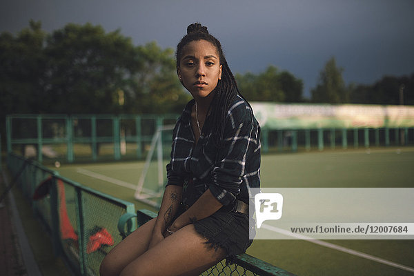 Ernste afroamerikanische Frau sitzt auf dem Zaun eines Sportplatzes