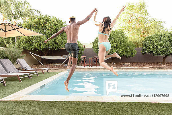 Couple holding hands jumping into swimming pool