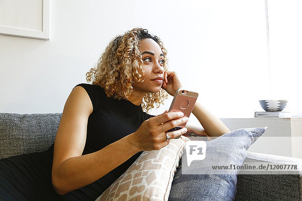 Mixed race woman laying on sofa holding cell phone