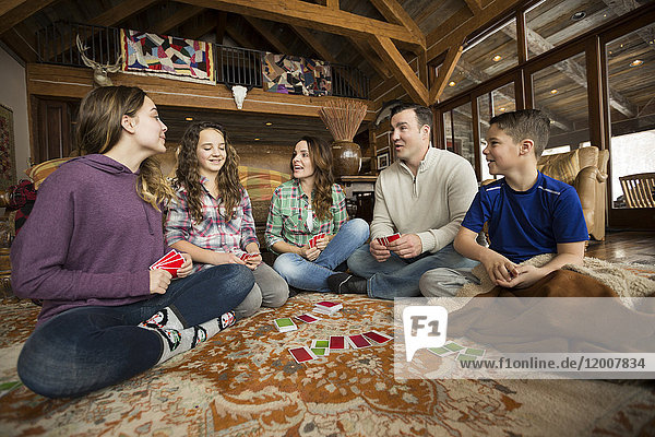 Kaukasische Familie sitzt auf einem Teppich und spielt ein Kartenspiel