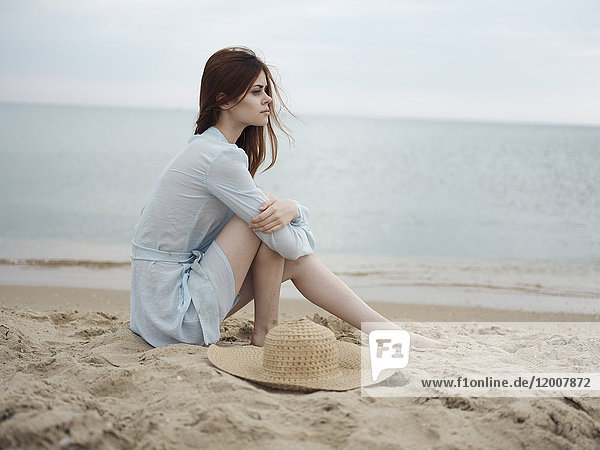 Nachdenkliche kaukasische Frau sitzt am Strand