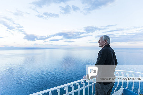 Kaukasischer Mann bewundert die Aussicht auf einem Balkon am Wasser