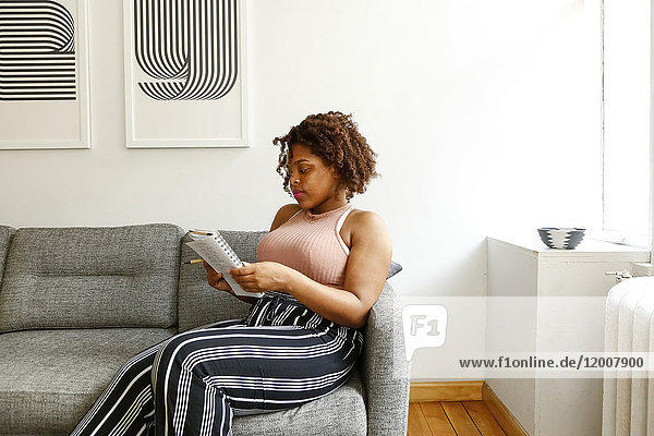 Gemischtrassige Frau liest auf dem Sofa in einem Notizbuch