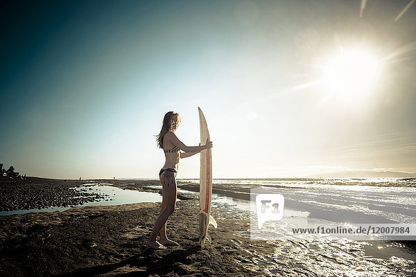 Kaukasische Frau steht am Strand und hält ein Surfbrett