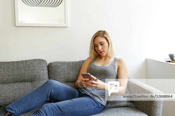 Kaukasische Frau sitzt auf dem Sofa und schreibt eine SMS auf ihrem Handy