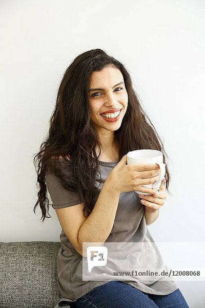 Gemischtrassige Frau auf Sofa trinkt Kaffee