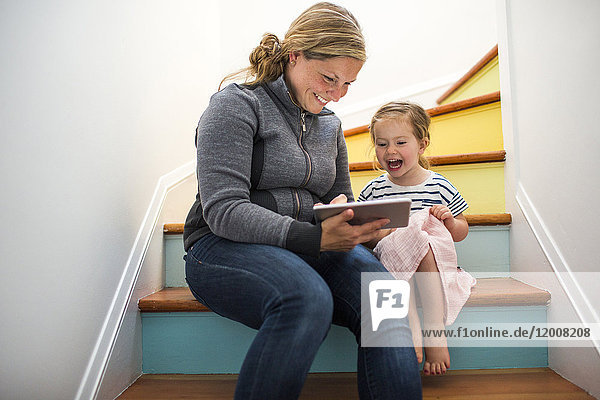 Kaukasische Mutter und Tochter benutzen ein digitales Tablet auf einer Treppe
