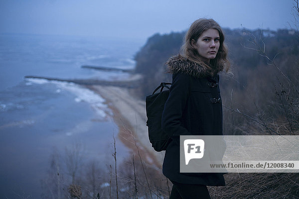 Kaukasische Frau mit Mantel auf einer Klippe in der Nähe des Ozeans