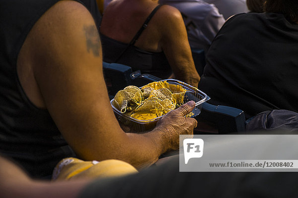 Mann sitzt im Stadion und isst Nachos