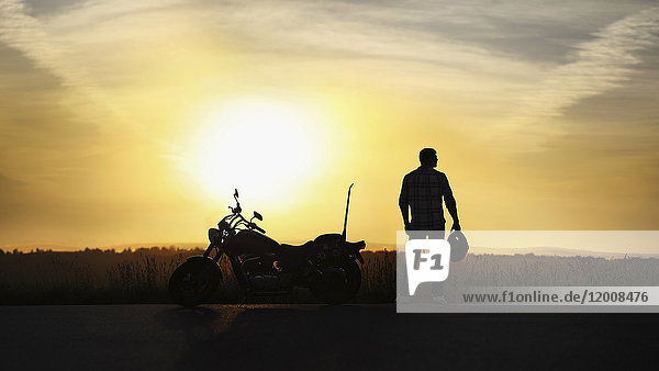 Silhouette eines Mannes mit Helm in der Nähe eines Motorrads bei Sonnenuntergang
