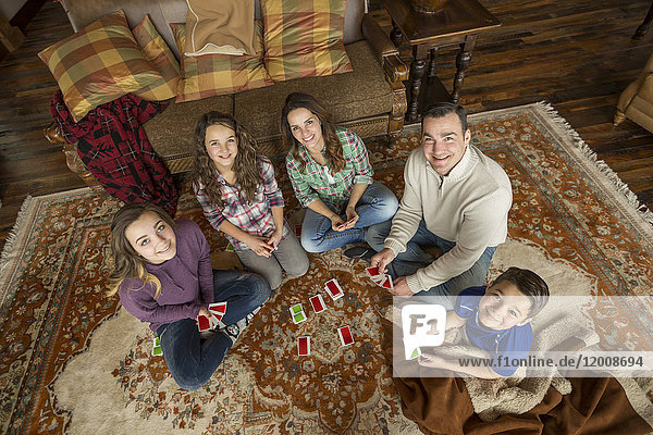 Porträt einer lächelnden kaukasischen Familie  die auf einem Teppich sitzt und ein Kartenspiel spielt