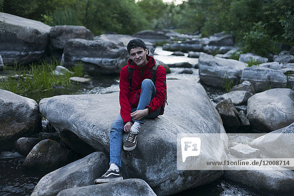 Kaukasischer Mann sitzt auf einem Felsen im Fluss