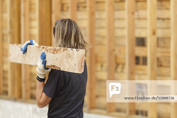 Caucasian woman carrying lumber at construction site