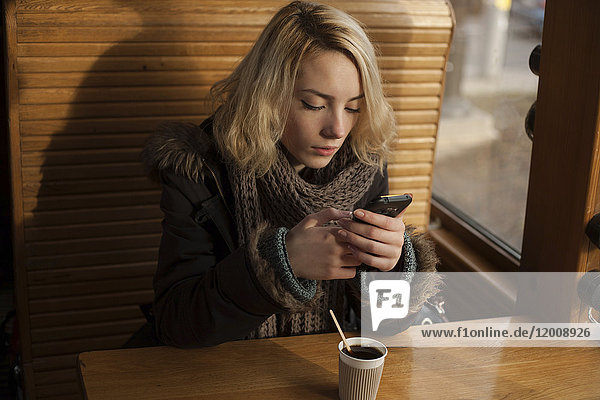 Kaukasische Frau trinkt Kaffee und schreibt eine SMS auf ihrem Handy