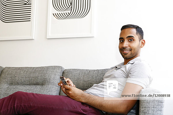 Mixed race man sitting on sofa texting on cell phone