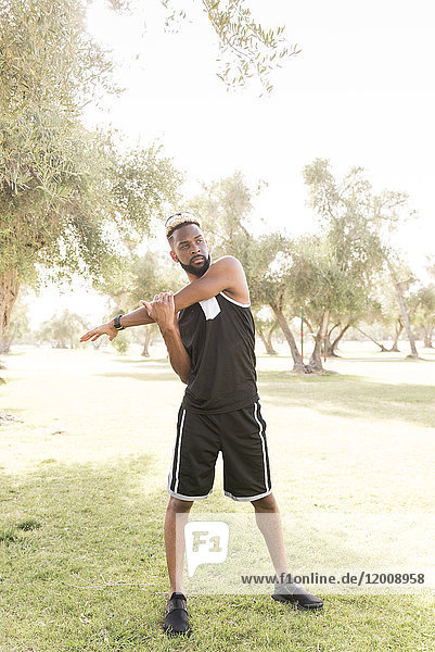 Black man standing in park stretching arm