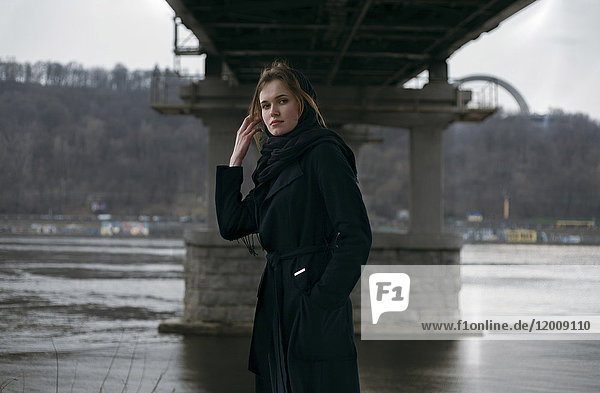 Kaukasische Frau steht unter einer Brücke in der Nähe eines Flusses
