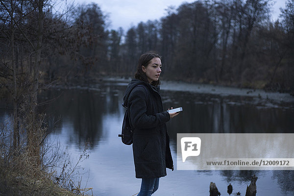 Kaukasische Frau hält Handy in der Nähe des Flusses