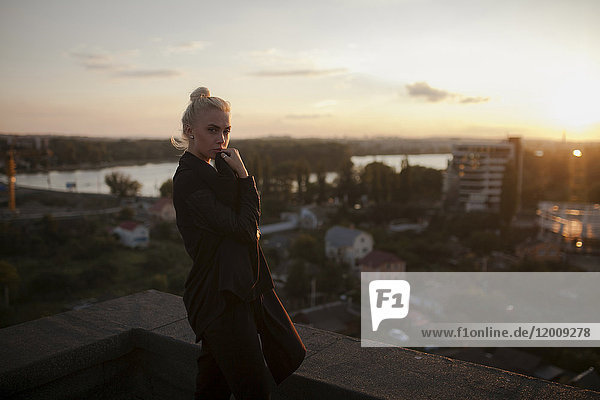Nachdenkliche kaukasische Frau auf dem Dach stehend bei Sonnenuntergang