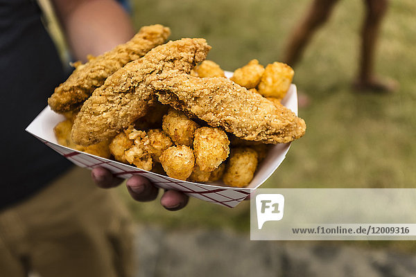 Hand holding container of fried chicken and potatoes