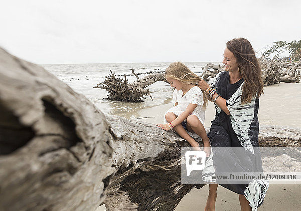 Kaukasische Mutter und Tochter sitzen auf Treibholz am Strand
