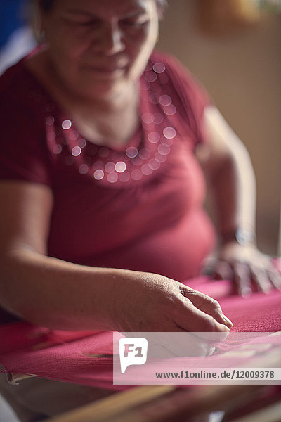 Hispanic woman weaving fabric on loom