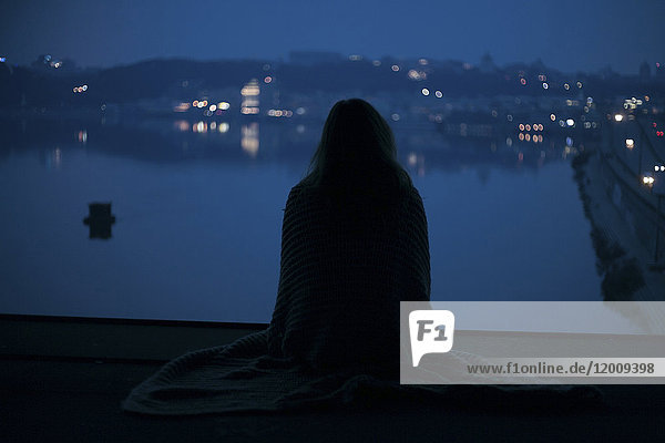 Kaukasische Frau sitzt nachts in der Nähe des Ufers